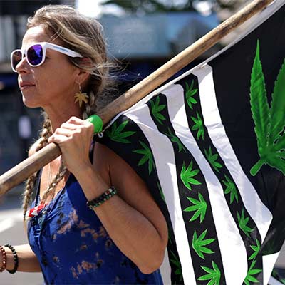 Eine Frau trägt eine Fahne mit Cannabis-Blättern, die symbolisch für die Freiheit des Cannabiskonsums steht.